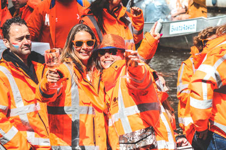 Amsterdam, Netherlands - April 27, 2019: Women on party boat dressed in national orange color celebrating the Kings day, Koningsdag, the birthday of the Dutch King Willem-Alexander. Raising glasses.のeditorial素材