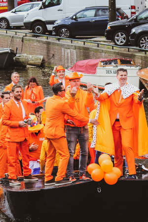 Amsterdam, Netherlands - April 27, 2019: Party boats on canal with people dressed in national orange color while celebrating the Kings day, Koningsdag, the birthday of the Dutch King Willem-Alexander.のeditorial素材