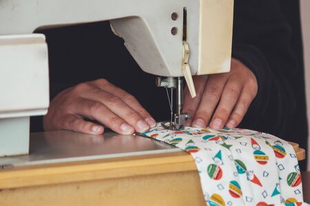Woman hands using the sewing machine to sew a colorful face medical mask during the coronavirus pandemic. Homemade DIY protective mask against the virus. Sewing masks, COVID-19. Selective focus.の写真素材