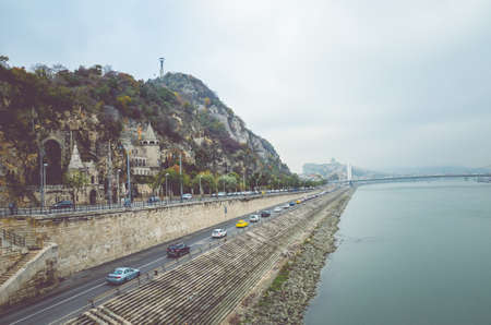 Budapest, Hungary - Nov 6, 2019: Gellert Hill Cave Church, Sziklatemplom. Liberty Statue on the top of the hill. Cars on the road in front of the hill by the Danube river. Hungarian landmarks.のeditorial素材