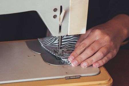 Woman hands using the sewing machine to sew the face medical mask during the coronavirus pandemic. Homemade protective mask against the virus. Sewing masks, COVID-19. Partly blurred, selective focus.の写真素材