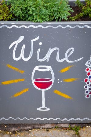 Handwritten sign wine and simple drawing of a wineglass with red wine and blue grapes. Original advertisements attracting people to buy wine. Vertical photo.の写真素材