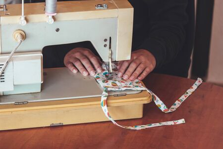 Woman hands using the sewing machine to sew a colorful face medical mask during the coronavirus...