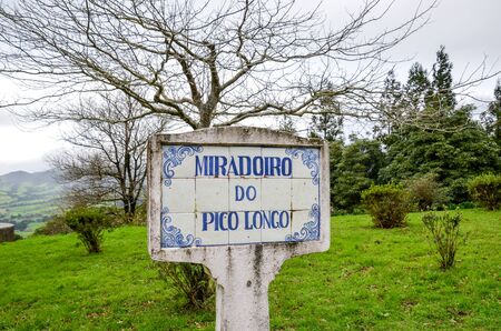 Blue sign Miradoiro do Pico Longo, Viewpoint Pico Longo in English, on typical Portuguese tiles. Grass and trees without leaves in the background. Horizontal photo.の写真素材