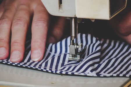 Woman hands using the sewing machine to sew a colorful face medical mask during the coronavirus pandemic. Homemade DIY protective mask against the virus. Sewing masks, COVID-19. Selective focus.の写真素材