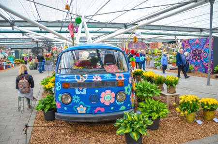 Keukenhof, Lisse, Netherlands - Apr 28, 2019: People walking inside of an exhibition house in Keukenhof gardens. Hippie van with hippies symbols, colorful flowers, and tourists walking around.のeditorial素材