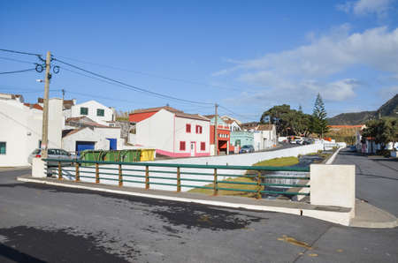 Mosteiros, Azores, Portugal - Jan 12, 2020: View of traditional Portuguese village in Azores Islands. Houses with colorful facades, asphalt road, river stream under the bridge. Horizontal photo.のeditorial素材