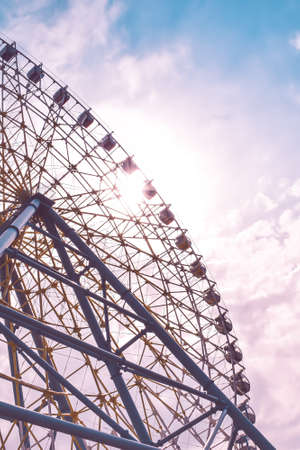 Ferris wheel in the amusement park photographed against the sun. Construction of the attraction with pink sky and clouds in the background. Adventure, holiday concept, conceptualの写真素材