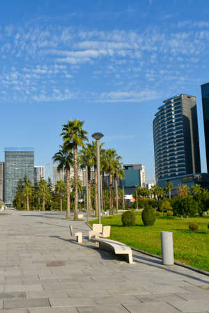 Batumi, Adjara, Georgia - Dec 6, 2021: Park on Lech and Maria Kaczynski Boulevard in the Georgian Black Sea resort. Legend Hotel in the background. Green trees and grass, blue sky, sunny day.のeditorial素材