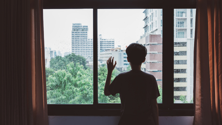 Someone standing by window with raindrops on a rainy dayの写真素材