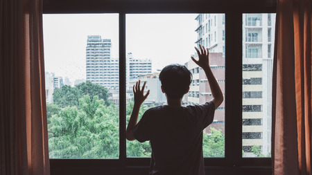 Someone standing by window with raindrops on a rainy dayの写真素材