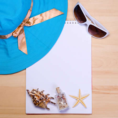 empty white notebook on wooden table surface with beach hat, seashells, starfish, sunglassesの写真素材