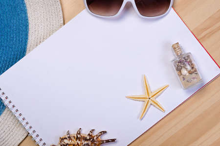 empty white notebook on wooden table surface with beach hat, seashells, starfish, sunglassesの写真素材