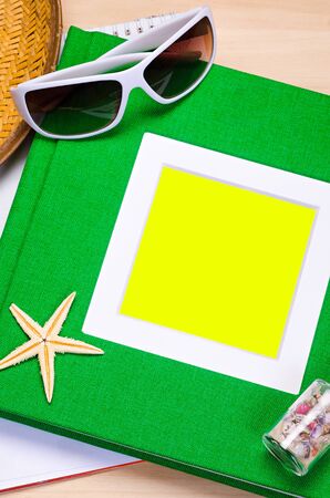 empty green notebook on wooden table surface with beach hat, seashells, starfish, sunglassesの写真素材