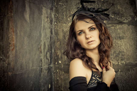 Beautiful young brunette woman in a vintage style in evening black dress on the street in the old...