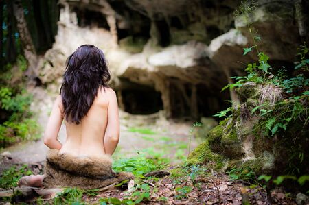 Beautiful young brunette woman wearing a wolf skin in the green forest near the ancient cavesの写真素材