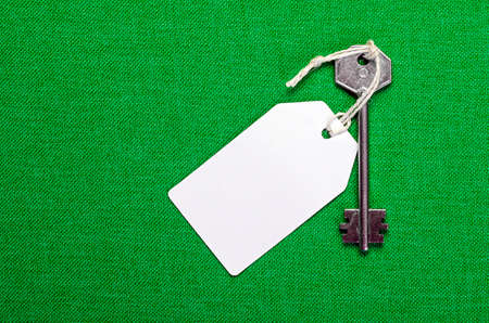 white paper tag attached to the metal silver key on the green backgroundの写真素材