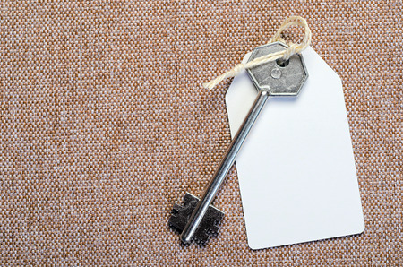 white paper tag attached to the metal silver key on the brown backgroundの写真素材