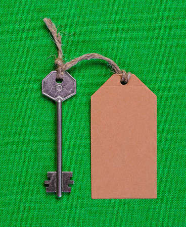 brown paper tag attached to the metal silver key on the green  fabric backgroundの写真素材