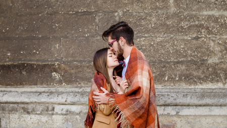 Young fashion elegant stylish couple standing, embracing, wrarps in pled on streets of old european cityの写真素材