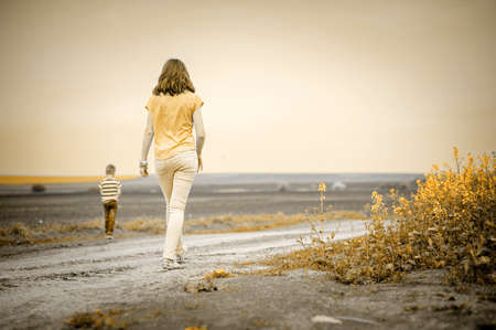 Young woman walking with son on rural road back to camera, vintage colorの写真素材