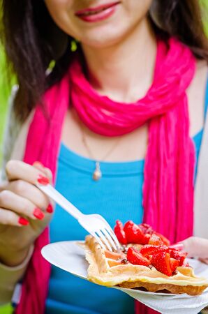 young girl in glasses eats waffles with strawberries, outdoorの写真素材
