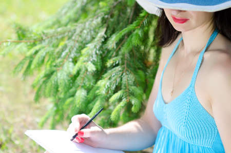 Beautiful young girl sitting on the green grass in the meadow, and draws from nature, focus on the lipsの写真素材