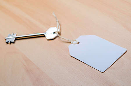 white paper tag attached to the metal silver key on the wooden backgroundの写真素材
