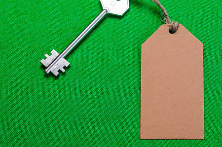 brown paper tag attached to the metal silver key on the green  fabric backgroundの写真素材