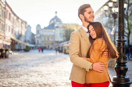 Outdoor lifestyle portrait of young couple in love standing in old town on the street behind sunsetの写真素材