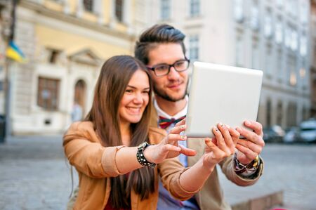 Young smile  couple sitting on stairs in summer , photographs selfie on tablet pc, focus on tablet pcの写真素材
