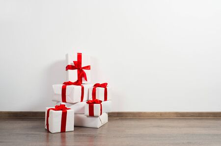 A pile of Christmas gifts in colorful wrapping with ribbons against the wall on a beautiful hardwood...