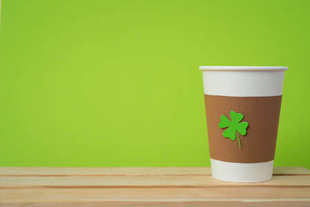 take away cup with cut and pasted green shamrock symbol on wooden desk with green wallの写真素材