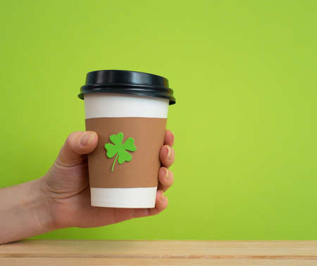 take away cup in a hand with cut and pasted green shamrock symbol on green backgroundの写真素材
