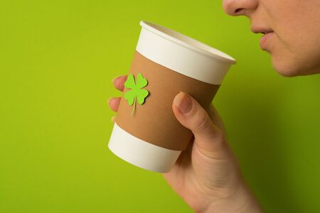 take away cup in a hand with cut and pasted green shamrock symbol on green backgroundの写真素材