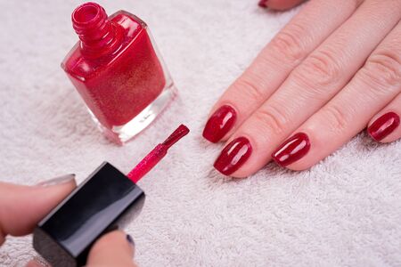 manicured woman's nails with red nail polish on white towel