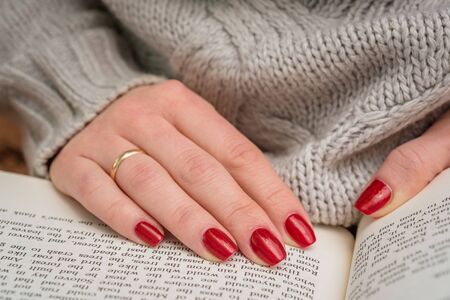 The girl in the knitted sweater sitting at the table reading a book. Closeup.の写真素材
