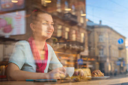 young woman is sitting at the cafe while drinking coffee, through glassの写真素材