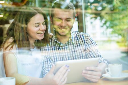 Flirting couple in cafe using digital tablet. looking through windowの写真素材