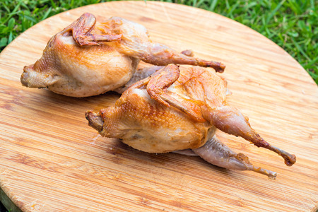 Roasted Partridge, quail on the wooden round board on green grass. Top view. Partridge on the wooden board on sunny day. Culinary concept.の写真素材