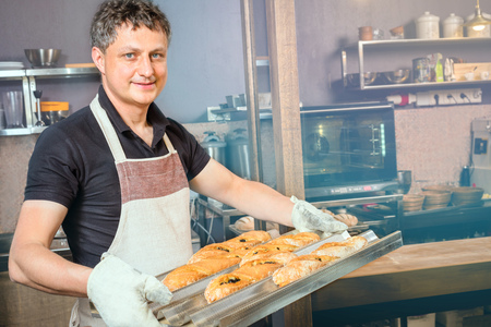 baker concept. Happy baker showing tray of fresh bread in the kitchen of the bakeryの写真素材