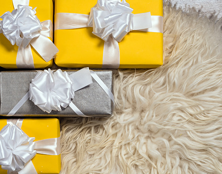 A pile of yellow and grey Christmas gifts in colorful wrapping with ribbons against the wall on a beautiful hardwood floor with copyspaceの写真素材