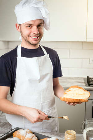 slile baker on kitchen with peanut butter on a slice of croissant in handsの写真素材