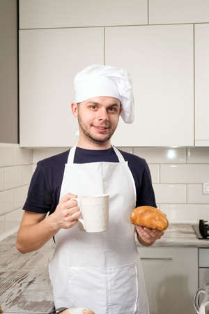 smiling baker hold a cup of tea and croissant in handsの写真素材