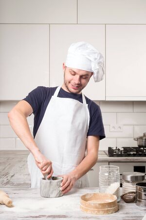 cook chef costume preparing the spices in a mortar on a white kitchenの写真素材