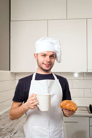 smiling baker hold a cup of tea and croissant in handsの写真素材