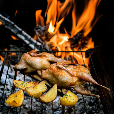Grilling delicious poultry quails in a restaurant on barbecue. Partridge, quail and potato prepared on the grill on sunny day. Culinary concept with delicious food.の写真素材