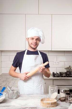cooking concept - happy male chef cook holding rolling pin with croissant on deskboardの写真素材