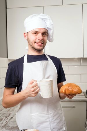 smiling baker hold a cup of tea and croissant in handsの写真素材