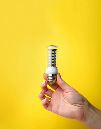 Hand holding LED bulb lamp on yellow background. Eco power concept.の写真素材
